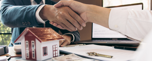 Close-up of a handshake over real estate documents and a miniature house model, symbolizing successful deals at CENTURY 21 Triangle Group.