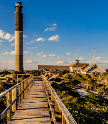 Oak Island Lighthouse standing tall at sunset, surrounded by coastal homes and greenery in Oak Island, NC.