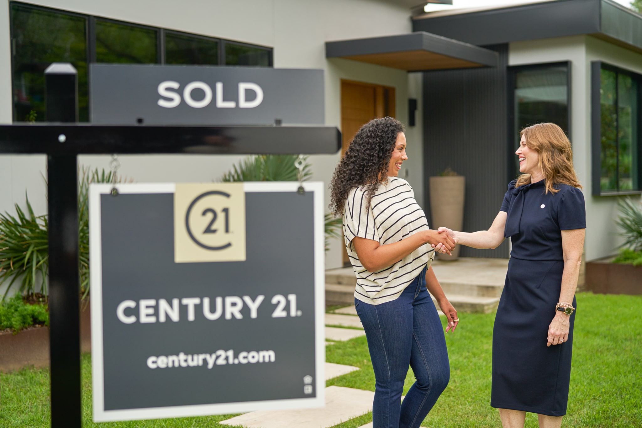 Real estate agent shaking hands with a client in front of a house with a Century 21 sold sign.